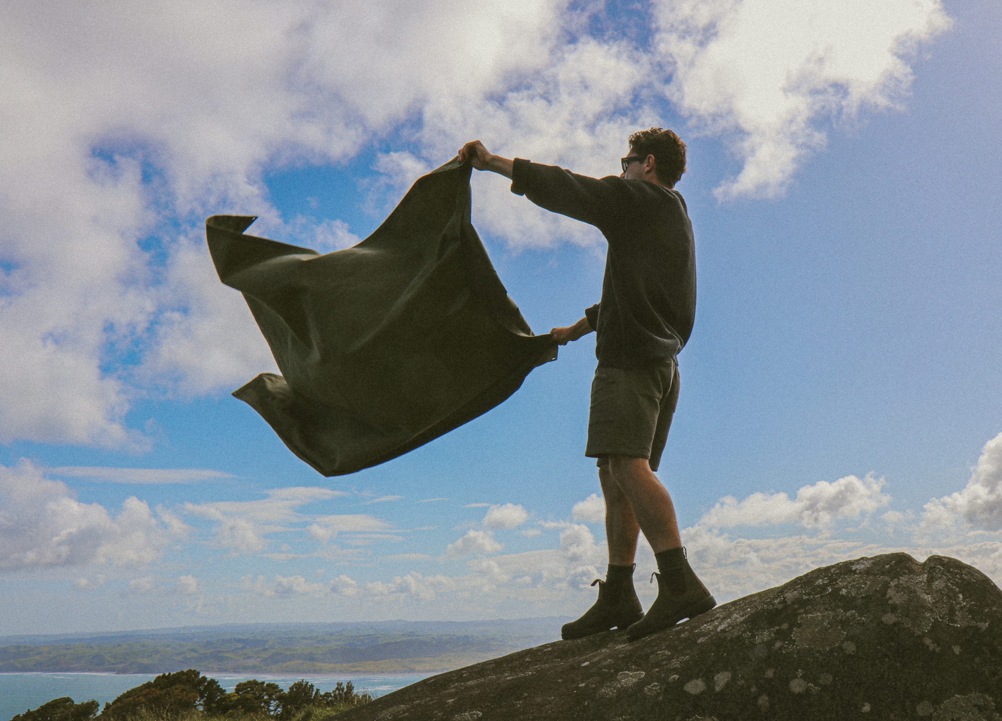 Person holding a large piece of waxed canvas fabric against a blue sky with clouds.