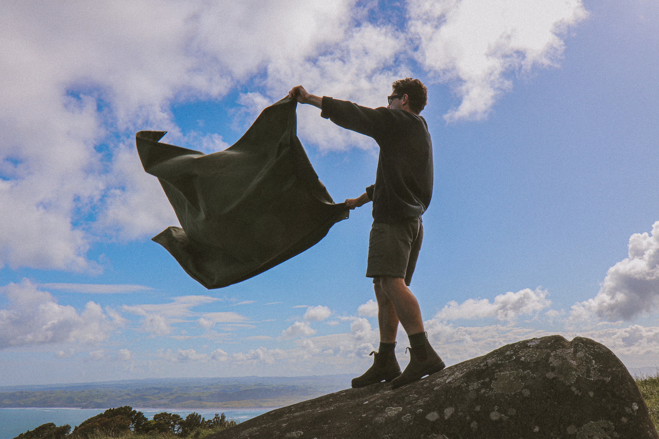 Person holding a large piece of waxed canvas fabric against a blue sky with clouds.