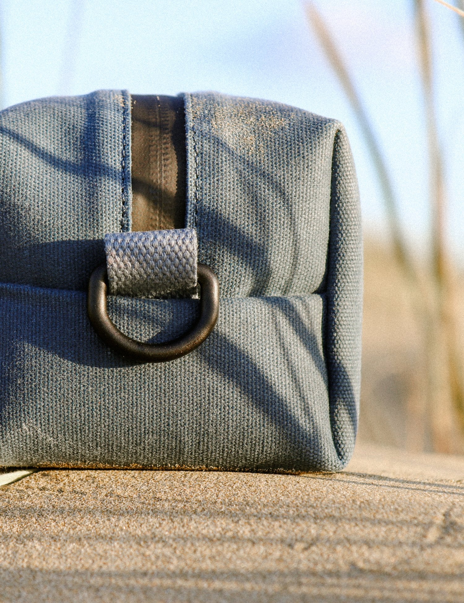 Canvas washbag with a aluminium buckle on a wooden surface with a blurred natural background