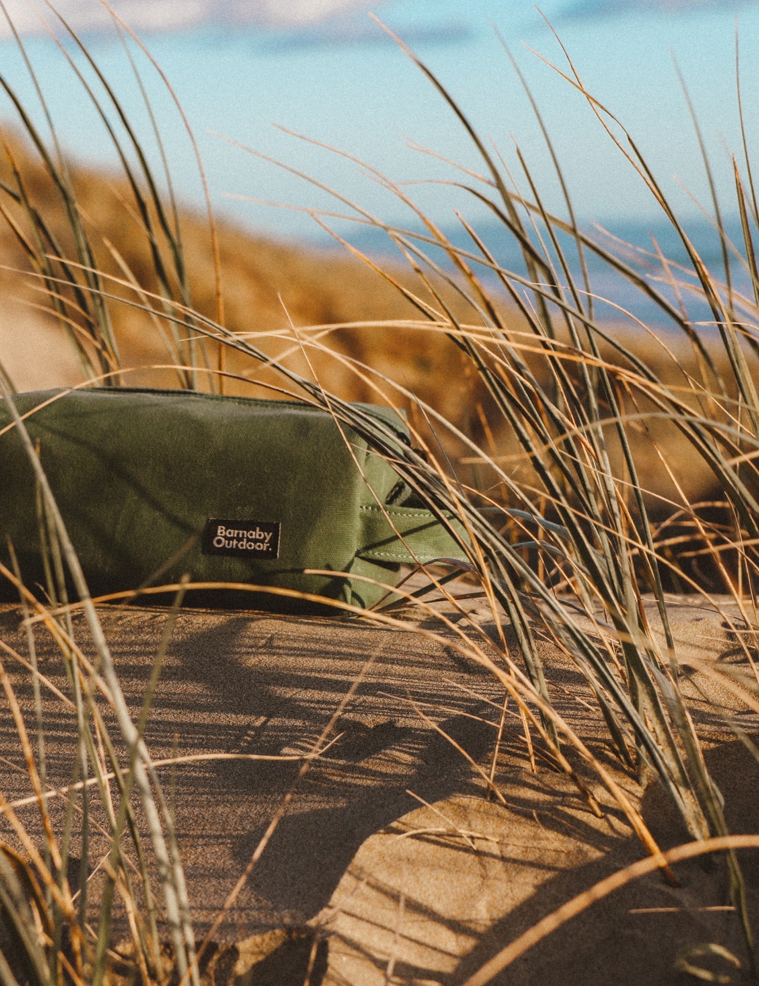 Green bag with a brand logo on a wooden surface surrounded by tall grass