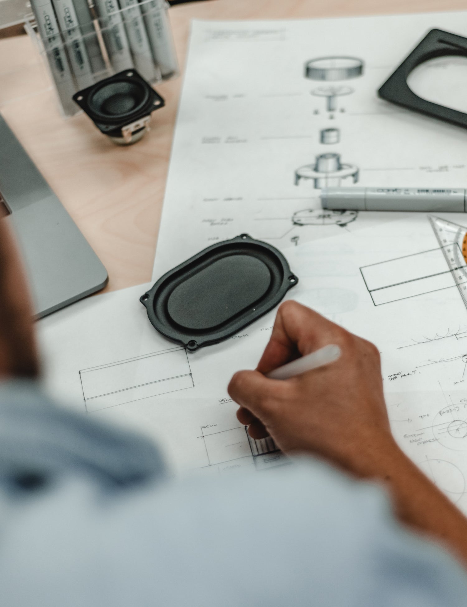 Person working on technical drawings with speakers and tools on a table