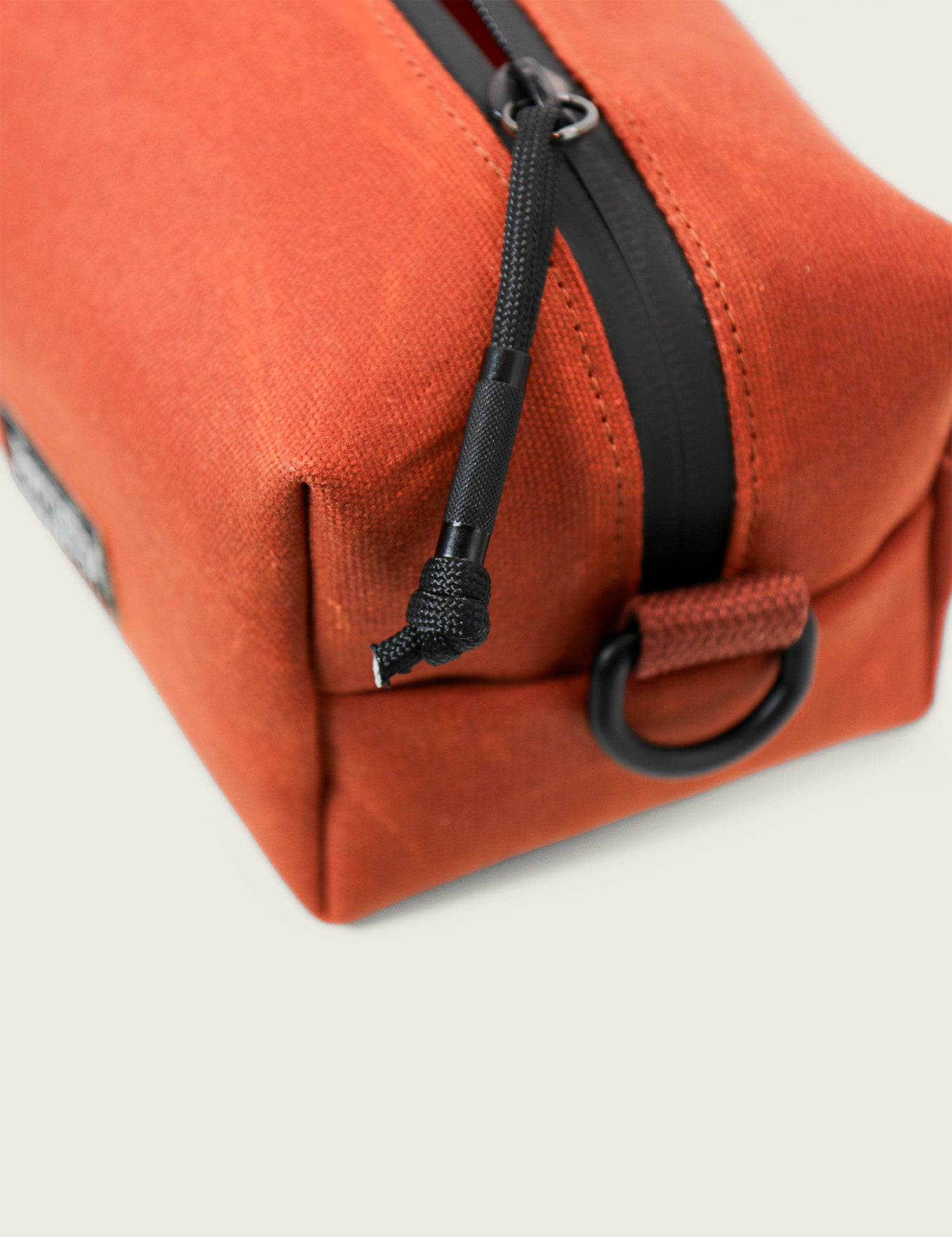 Close-up of an orange toiletry bag with a black zipper on a light gray background